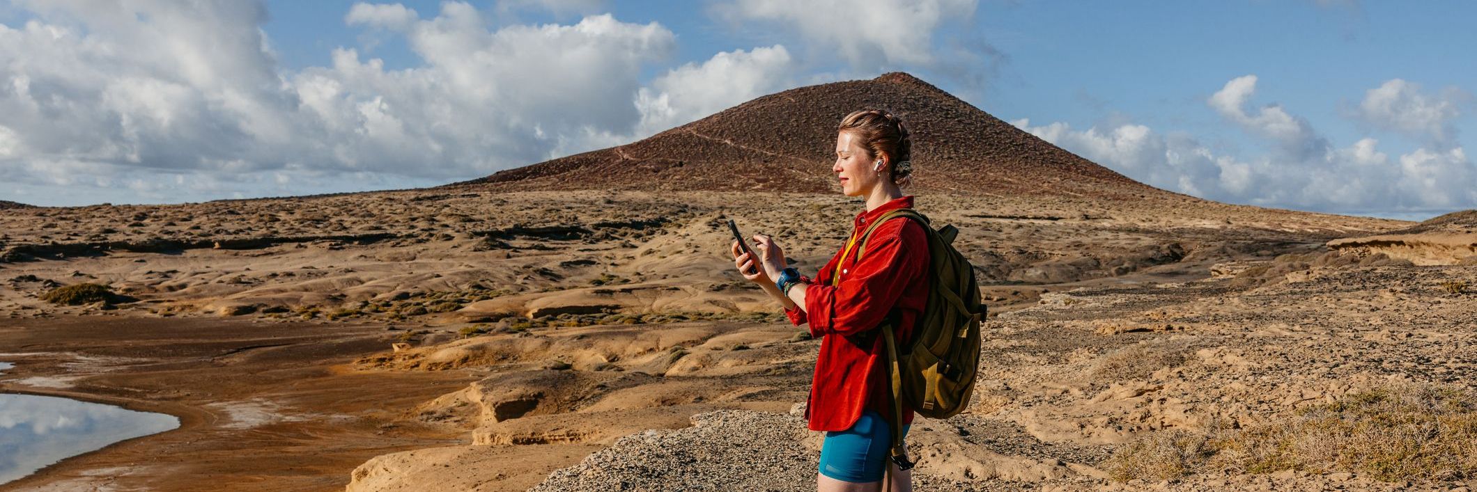 Young woman checking fitness activity on the phone while listening to music after completing a hike on the Tenerife island in Spain.