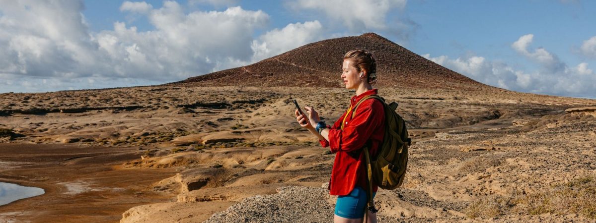 Young woman checking fitness activity on the phone while listening to music after completing a hike on the Tenerife island in Spain.